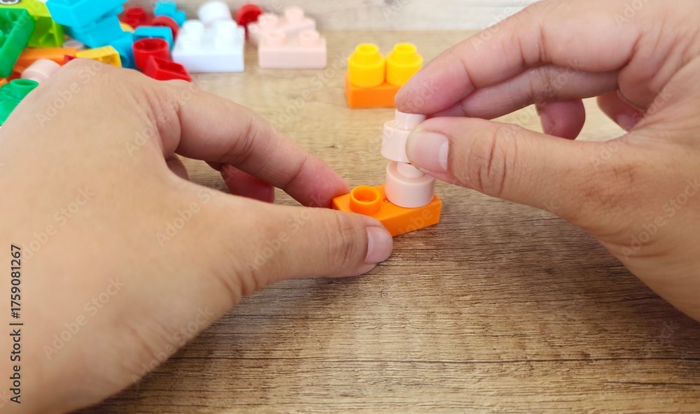 Fototapeta premium an asian woman is playing with lego forming the legs to form a giraffe with a brown background