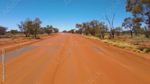 View of a red dirt road through arid landscape under clear blue sky