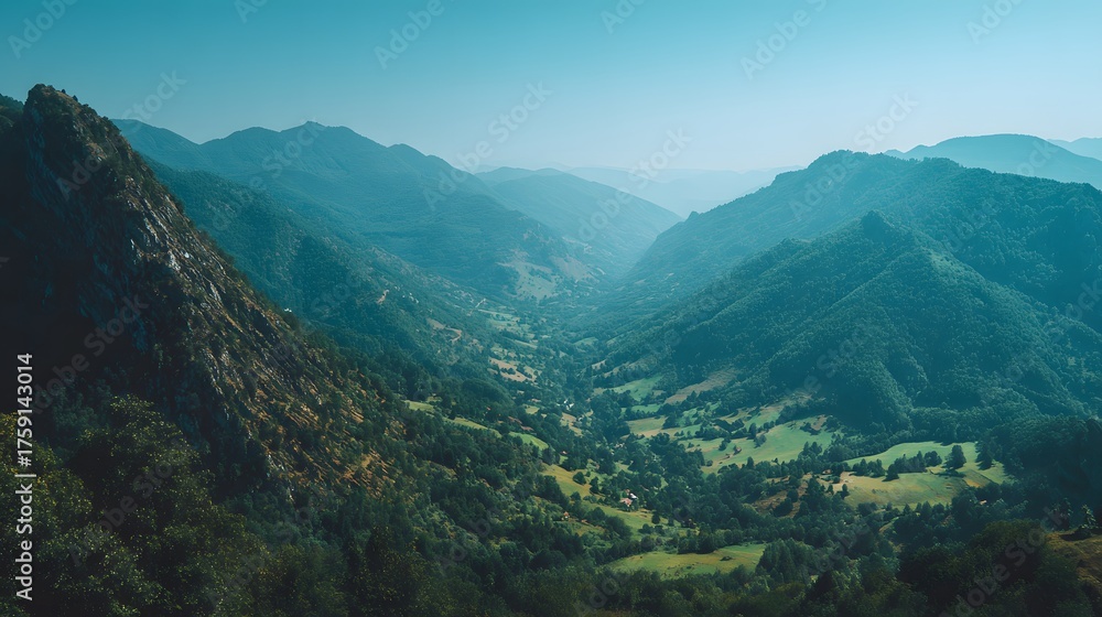 Fototapeta premium Lush green valley nestled between misty mountain ranges under a clear sky.