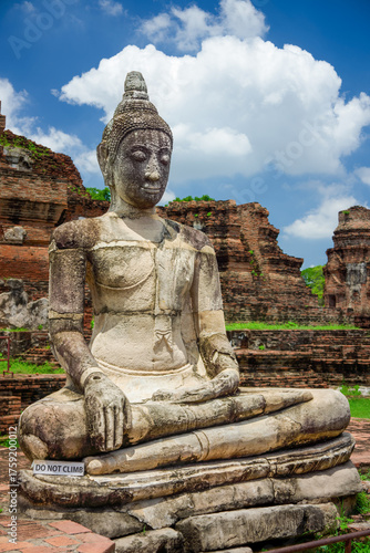 Ancient Buddha Statue and Wat Mahathat Ruins in Ayutthaya Historical Park. Weathered stone Buddha statue seated amongst the majestic brick ruins at UNESCO World Heritage Site in Ayutthaya, Thailand.