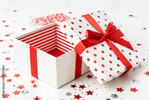 Open gift box with red ribbon, polka dots and festive star confetti
