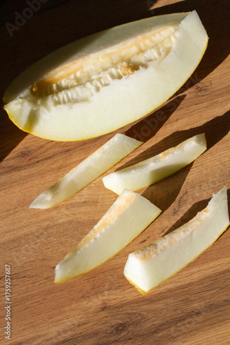 slices of cut melon on a wooden surface in sunlight, viewed from above