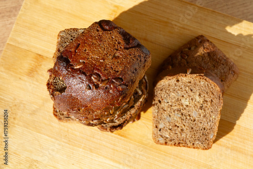 sliced bread piled up in a pyramid next to 2 pieces of bread with crust and seeds on it on a wooden surface, viewed from above