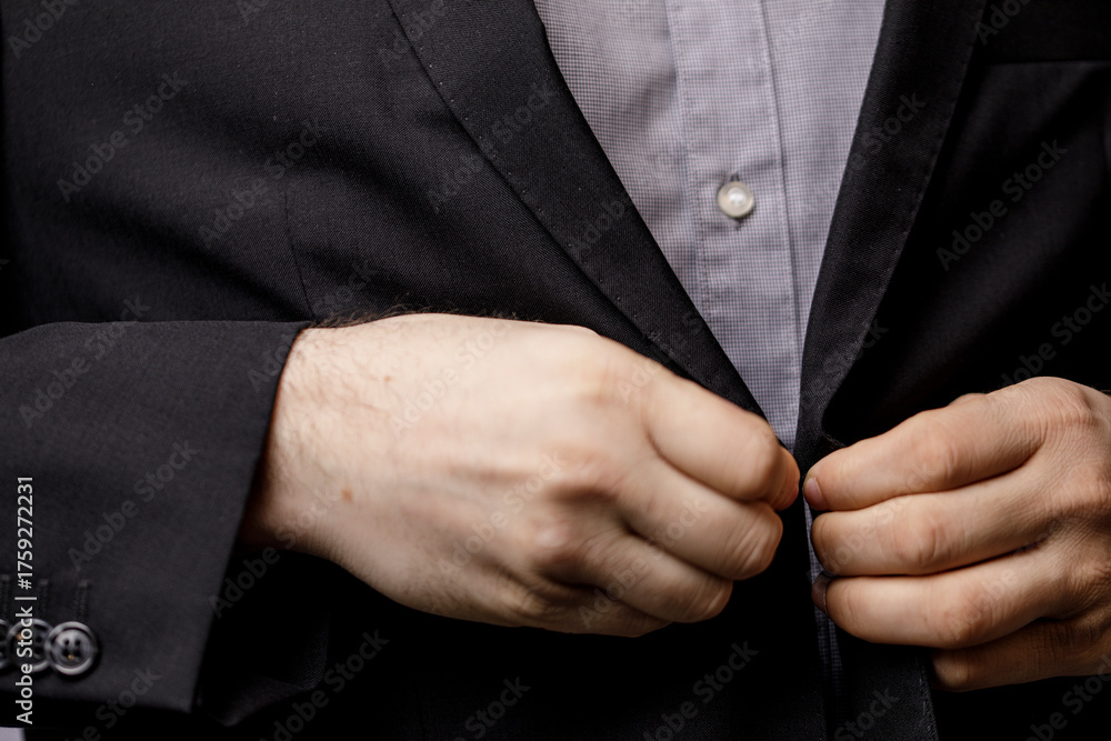 Obraz premium Detail of a man's hands buttoning his black suit jacket over a gray shirt. Suitable for business, corporate, or fashion-related content.