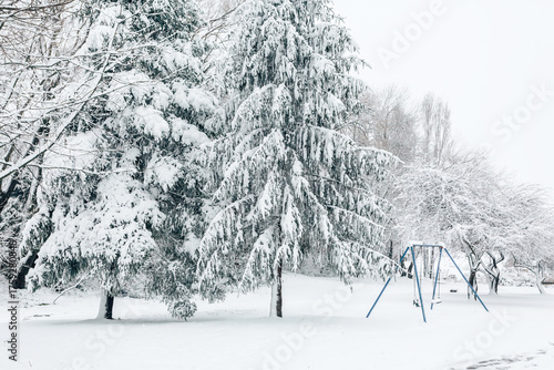 Snow covered trees and a child swing in a park
