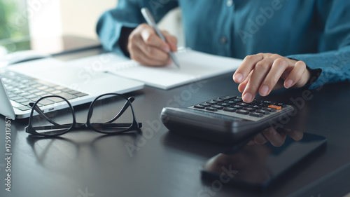 Close up woman hand using calculator to calculate home finance and writing note, accounting on table, budget management. Doing finance, budgeting and tax calculation, monthly expenses