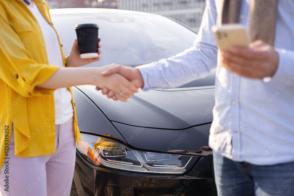 © sofiko14 - Two people shaking hands in front of a sleek black car, one holding a coffee cup, the other a phone. © sofiko14 - Two people shaking hands in front of a sleek black car, one holding a coffee cup, the other a phone.