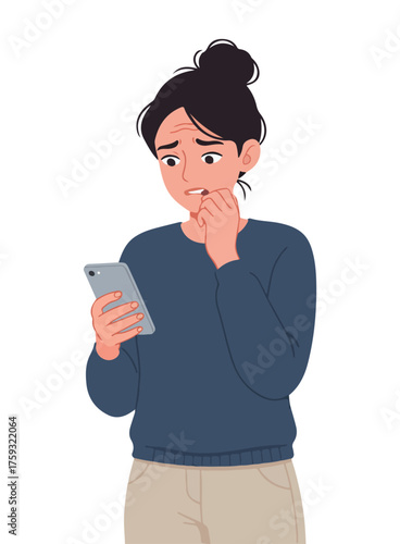 Young woman with dark hair tied up in a bun, looking worriedly at her smartphone screen, biting her nails.