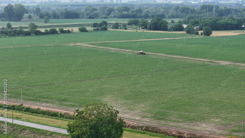 Obraz premium Aerial perspective showcases a dedicated farmer skillfully operating a tractor amidst a vast soybean field meticulously applying essential pesticides for crop protection and enhanced yield