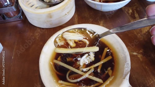 Delicious Thai-style braised fish maw soup served in a white bowl on a wooden table. Traditional Asian comfort food made with chicken, mushrooms, and thick brown broth, often found in street food stal