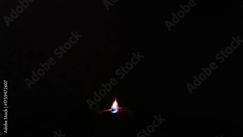 Slow-motion horizontal shot from India, a hand delicately lights a diya against a black background, capturing the essence of spiritual preparation and the vibrant warmth of Diwali festival celebration