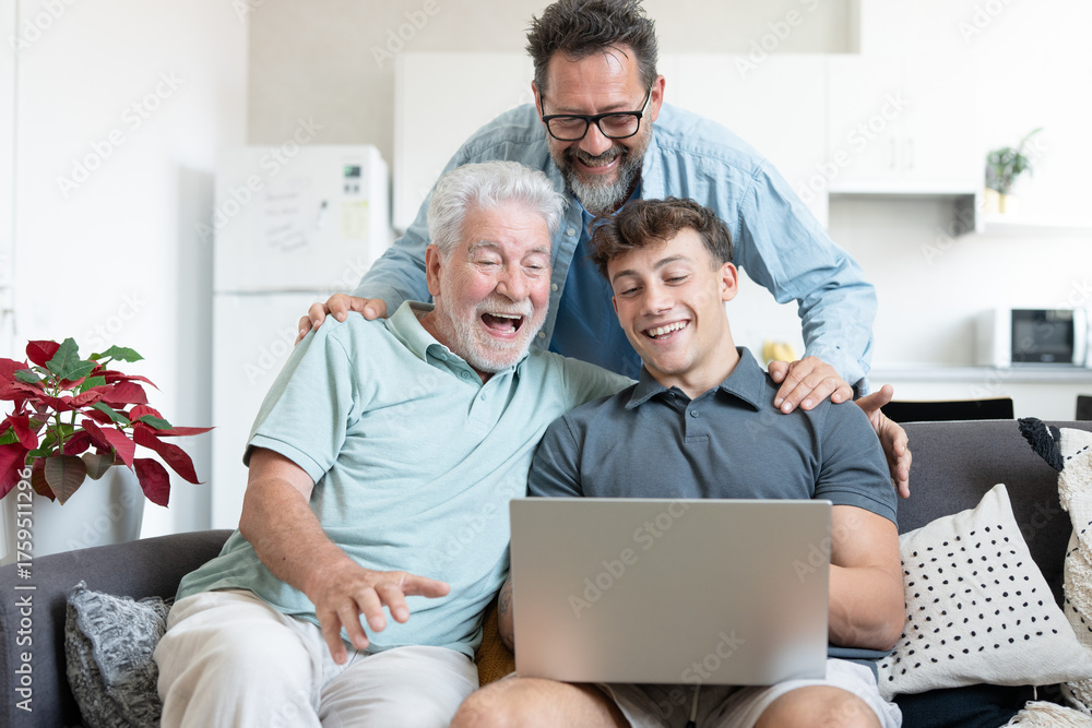 Obraz premium Three generations of men, grandfather, father, and son sitting together on sofa, laughing and enjoying time while using laptop at home, symbolizing family bonding and connection across generations