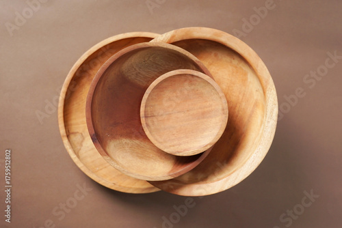 The image shows a stack of wooden bowls arranged neatly against a brown backdrop.