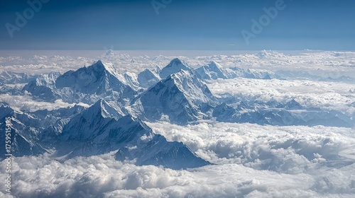 A breathtaking aerial view of snow-capped mountain peaks rising majestically above a sea of clouds under a clear blue sky.
