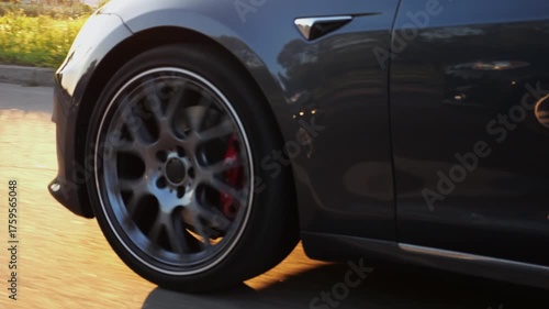 Wallpaper Mural Wheel of modern electrical automobile driving at urban road on sunny day. Ecology friendly car riding moving along motorway. Electric vehicle riding through empty highway. Green innovation concept Torontodigital.ca