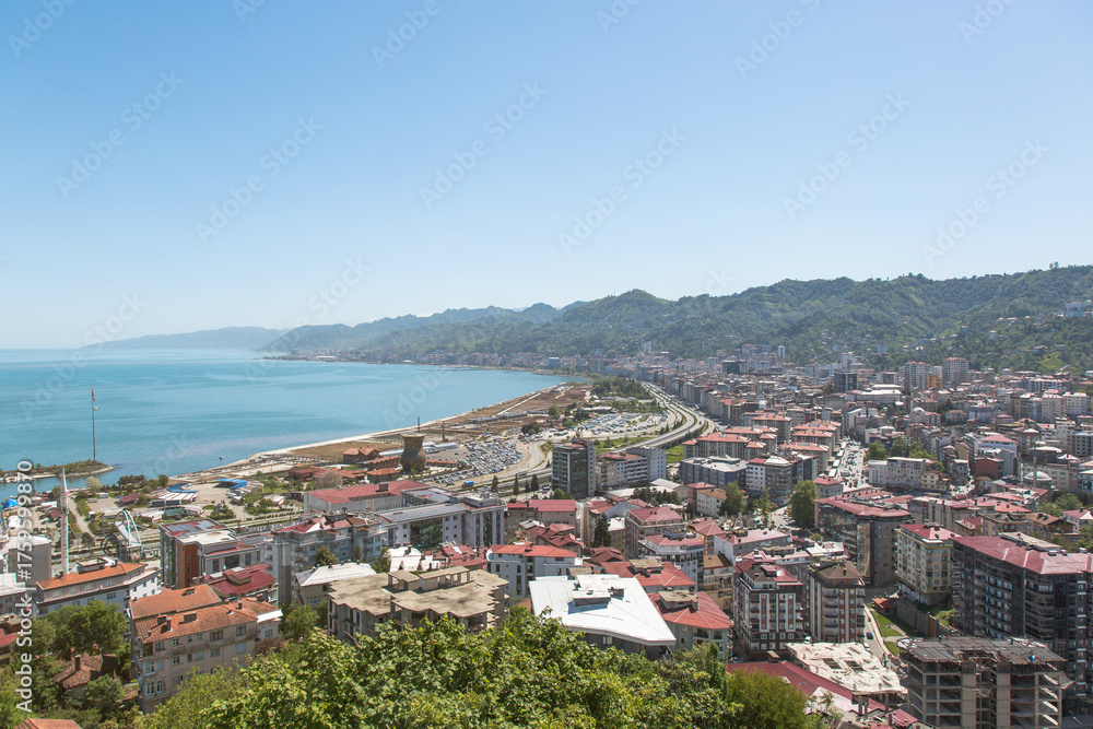 Obraz premium Aerial view of Rize city on the Black Sea coast with red-roofed buildings, highway and green hills, representing modern urban life, tourism and coastal landscape of northern Turkey