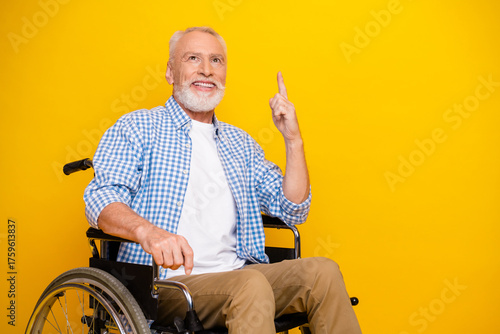 Cheerful grandpa in a wheelchair points to a bright idea while smiling against a bold yellow background bringing hope and humor to rehab and everyday health