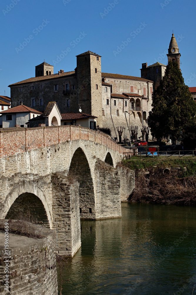 Obraz premium Monastero Bormida in Piedmont, Italy. An ancient Italian town with a historic stone bridge over the river surrounded by spring greenery. A peaceful and scenic landscape rich in heritage.