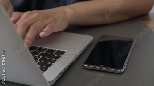 man typing on laptop beside smartphone on desk in office workspace, closeup of hand using technology in productive environment