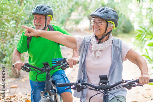Fotografie Two happy old mature people enjoying and riding bikes together to be fit and healthy outdoors