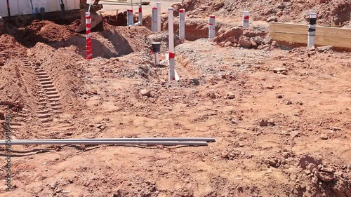 Groundwork for new structure is in progress with soil disturbed markers laid out plumbing pvc pipes