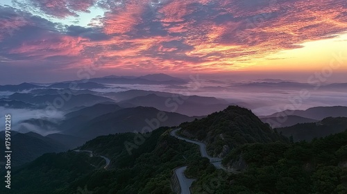A winding mountain road ascends through misty peaks under a vibrant sunset sky, capturing the serene beauty of nature's grandeur.