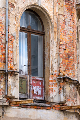 Weathered arched doorway with old wooden door, destroyed balkony, peeling paint and exposed brick