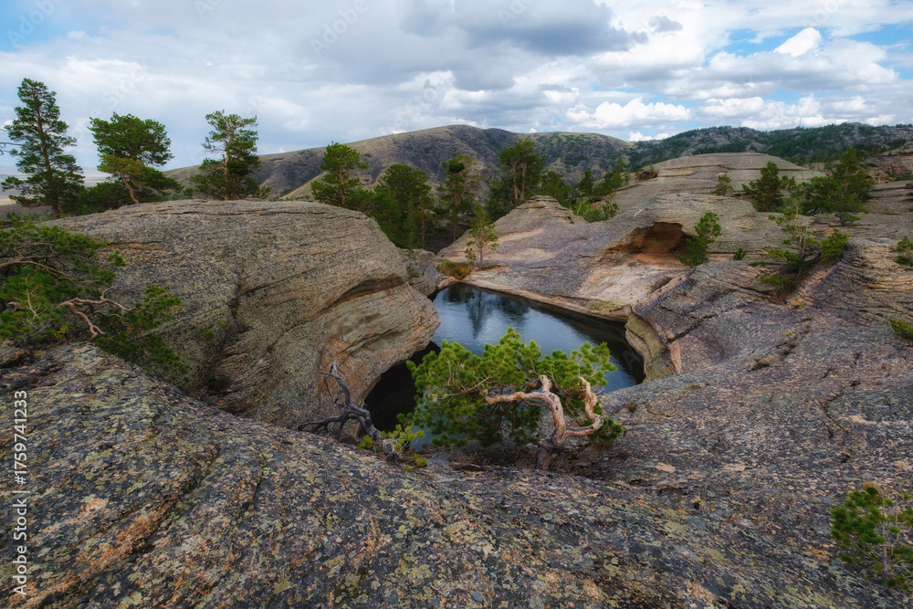 Obraz premium A mountainous landscape with a picturesque lake surrounded by rocky shores and sparse pine trees, located at the top of the Kent Mountains in Karkaraly Nature Park, this place is known as Forty Lakes.