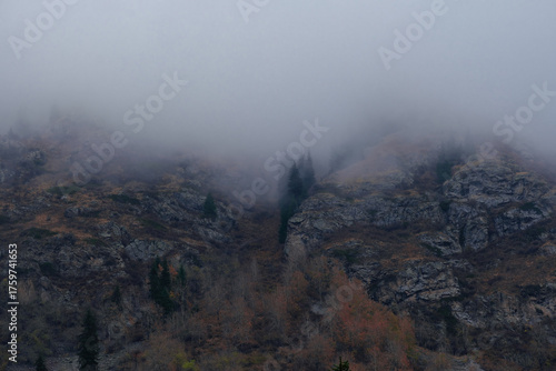A gloomy and foggy autumn landscape overlooking rocky mountains and a gorge shrouded in thick cloud. Dark, mysterious, and atmospheric.