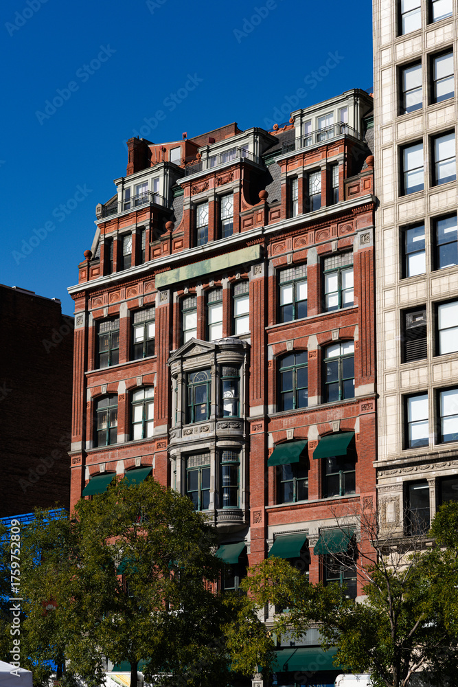 Fototapeta premium A large brick building with a green awning and a clock on the side. The building is surrounded by trees and has a lot of windows
