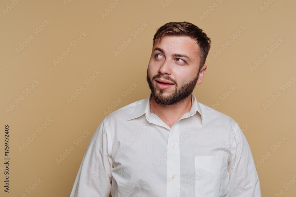 Obraz premium Man with beard wearing a white shirt gazes thoughtfully toward the side against a solid background