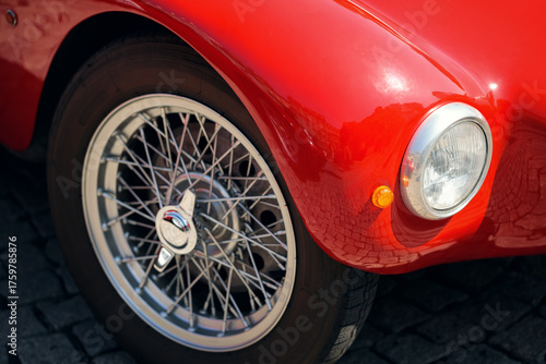 Close-up of a wire wheel and circular chrome headlight on a glossy red classic car fender.