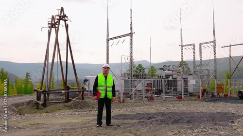 Electrical engineer is standing in front of distribution transformers. Engineer is working with distribution transformer at power station. Engineer is supervising power distribution transformers
