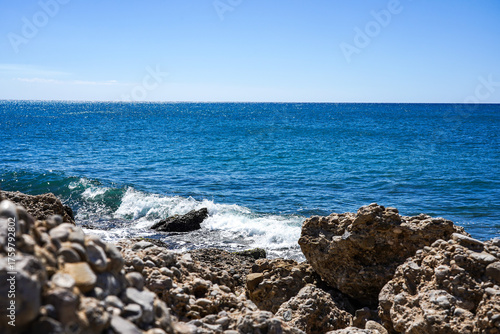 A Serene Coastal View with Clear Blue Waters and Rocky Shoreline Under Bright Sunshine on a Perfect Day