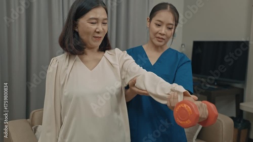 asian female caregiver assisting senior woman with physical therapy exercise at home during rehabilitation process to improve mobility strength and overall health care support in daily life