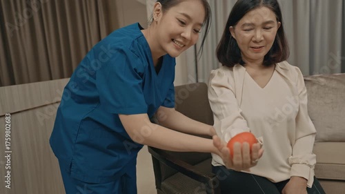 asian female caregiver assisting senior woman with physical therapy exercise at home during rehabilitation process to improve mobility strength and overall health care support in daily life