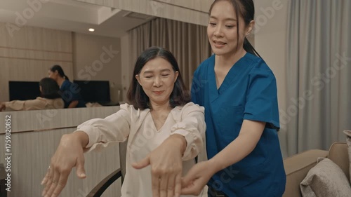 asian female caregiver assisting senior woman with physical therapy exercise at home during rehabilitation process to improve mobility strength and overall health care support in daily life