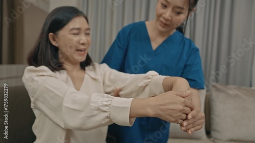 asian female caregiver assisting senior woman with physical therapy exercise at home during rehabilitation process to improve mobility strength and overall health care support in daily life