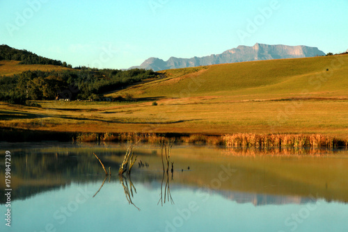 Beautiful landscape photo of a dam on an early misty morning, trees, mountains in the background, and reflections in the blue water.