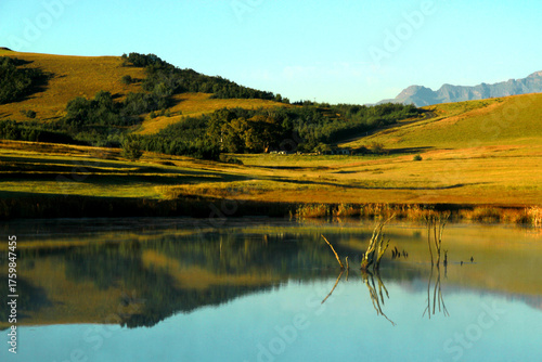 Beautiful landscape photo of a dam on an early misty morning, trees, mountains in the background, and reflections in the blue water.