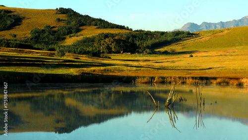 Beautiful landscape photo of a dam on an early misty morning, trees, mountains in the background, and reflections in the blue water.
