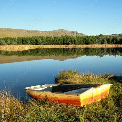 Beautiful view of a dam early in the morning with a colorful boat in front. The mountain and trees are reflected in the dam. 