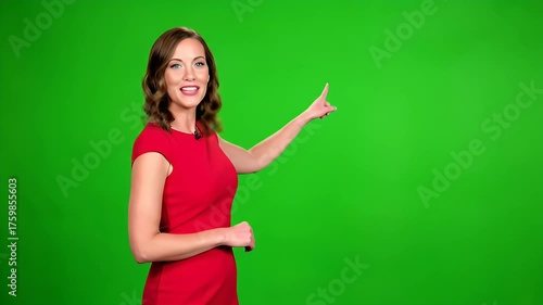 Smiling professional woman in red dress presenting on green screen, pointing to content. Female presenter on chroma key background.