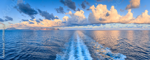 A glimpse of the Sicilian coast near Palermo at dawn, with orange clouds reflected in the sea crossed by a ship's wake, Italy.