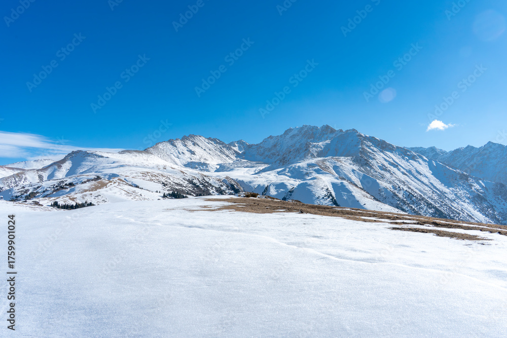 Fototapeta premium Snow-covered mountain peaks near the top ski lift station of Karakol ski resort in the Tian Shan mountains of Kyrgyzstan.