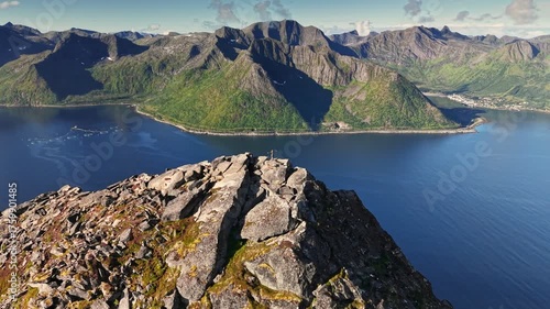 Man on top of mountain Segla, Senja island. Hiker reach the summit and admire breathtaking views of mountains and water in Norway. Aerial drone shot with orbit motion 
