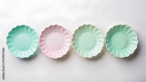 Four pastel colored oval scallop edge small plates arranged in a row on a white textured background for food presentation or decoration