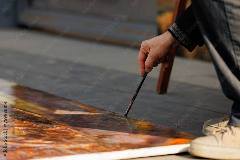 Obraz premium An artist skillfully adds vibrant strokes to a large canvas while seated on the ground, enjoying a sunny day.