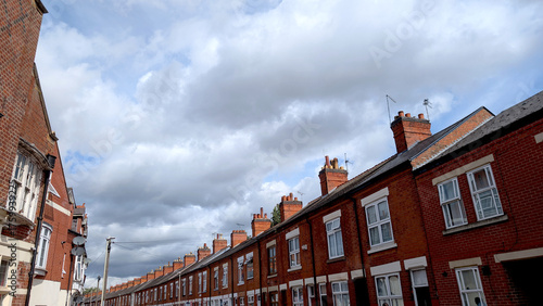 Long row of traditional English terraced houses made of classic red brick under a dramatic cloudy sky, great for themes of UK property and urban life