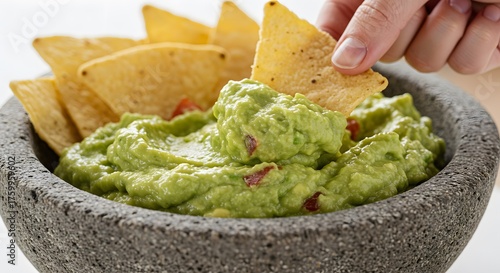 Vibrant green guacamole with a chip dipping in, set against a bright neutral background